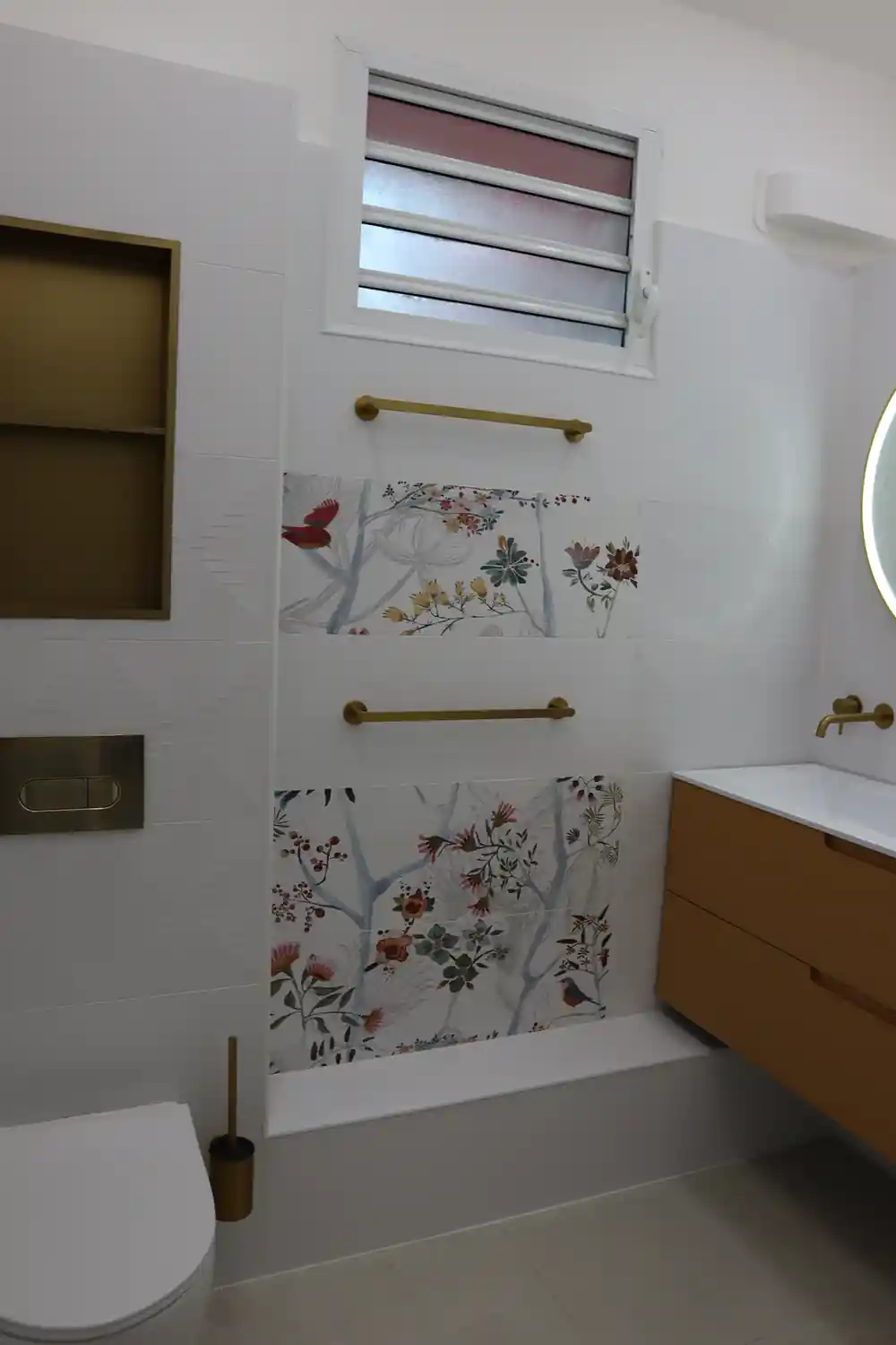 Carrelage décoratif fleuri et porte-serviettes dorés dans une salle de bain rénovée en Guadeloupe